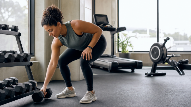 Lifter choosing dumbbells in a bright gym for a health news story about resistance training and longevity